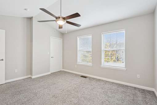 A room with a ceiling fan and two windows.
