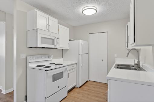 A white kitchen with a stove, microwave, refrigerator, and sink.