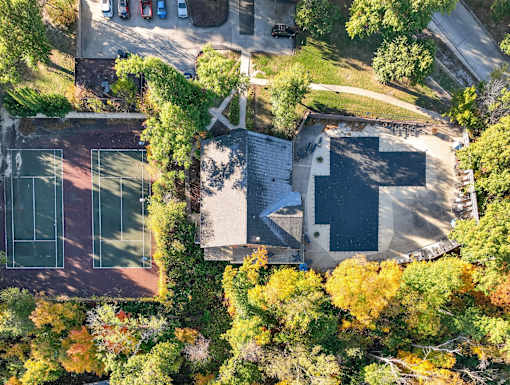 A tennis court is surrounded by trees and a building.