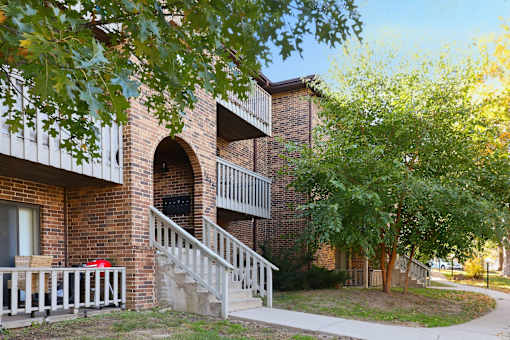 A red car is parked by a building with a white railing.