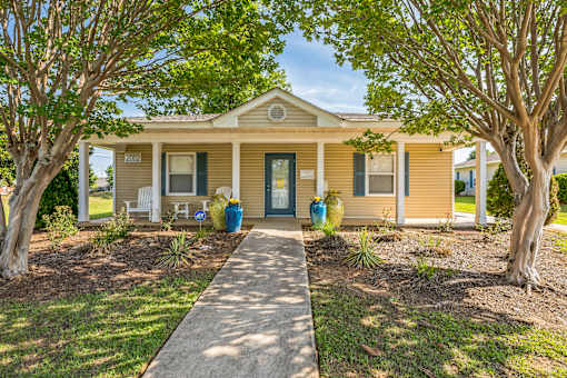 A yellow house with a porch and a tree in front.