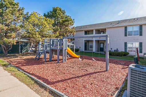 A playground with a slide and swings in front of a building.