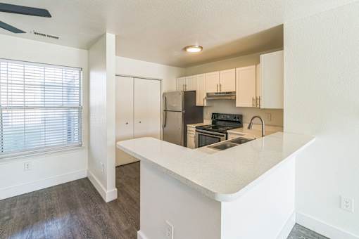 A kitchen with white countertops and a window with blinds.