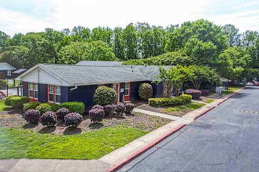 A house with a red trim and a grey roof is surrounded by greenery.