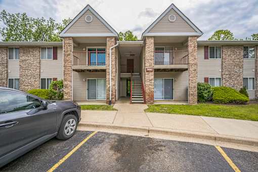 A grey car is parked in a parking lot in front of a two-story apartment building.