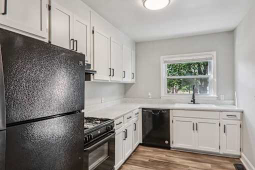 A black refrigerator in a kitchen with white cabinets and a window.