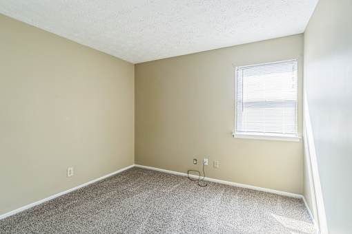 A room with a carpeted floor and a window with blinds.
