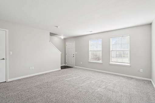 A spacious room with a carpeted floor and a staircase leading to another room.