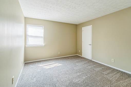 A room with a carpeted floor, a door, and a window.