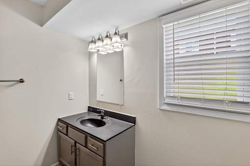 A bathroom with a sink, mirror, and window with blinds.