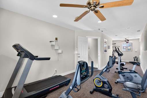 A spacious home gym with a treadmill, elliptical machines, and a fan.