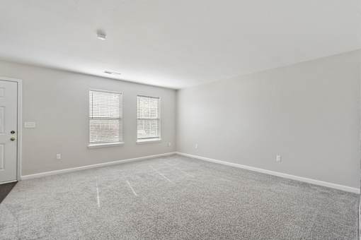 A room with a carpeted floor, two windows with blinds, and a door.