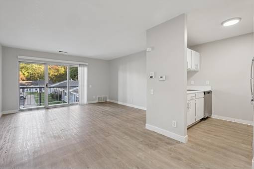A spacious room with wooden flooring and a kitchen area in the background.