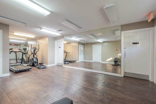 A spacious gym with treadmills, elliptical machines, and mirrors.