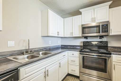 A kitchen with a stove, sink, and cabinets.