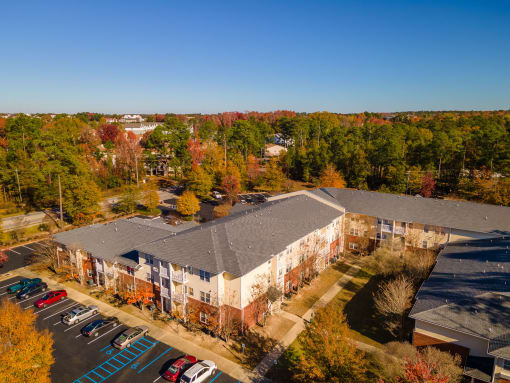an aerial view of a building with a parking lot and trees in the background