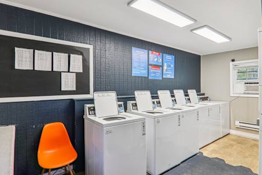 A room with a row of washing machines and a chair.