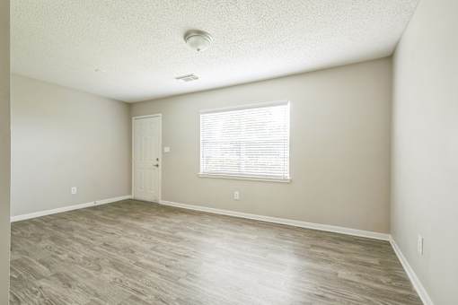 A room with a wooden floor and a window with blinds.