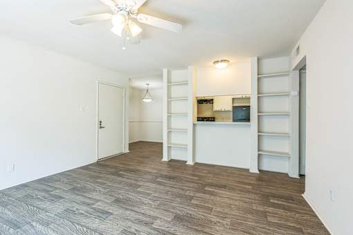 A room with a ceiling fan and a kitchenette in the background.