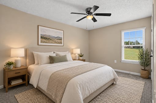 A bedroom with a large bed, a ceiling fan, and a window with a view of a green field.