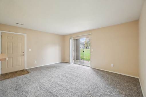 A room with a carpeted floor and a sliding glass door leading to a backyard.