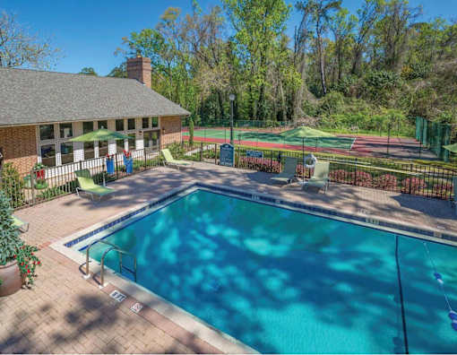 A pool surrounded by a fence with a tennis court in the background.