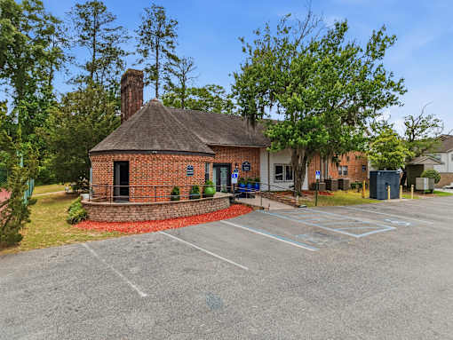 A small brick building with a black door and a chimney sits in front of a parking lot.