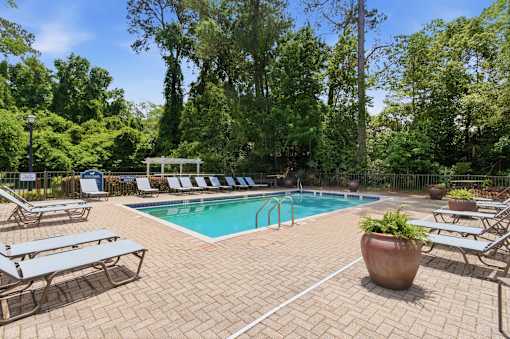 A pool surrounded by trees and lounge chairs.
