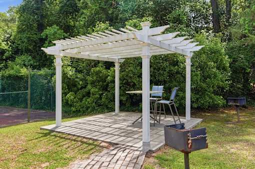 A white pergola with a grill underneath it.