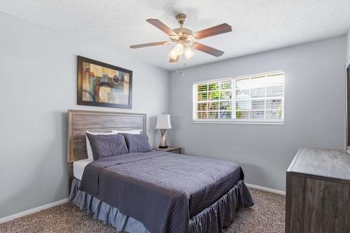 A bedroom with a bed, a ceiling fan, and a window with blinds.