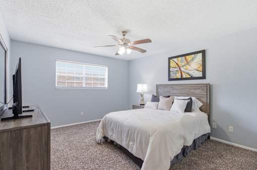 A bedroom with a bed, a television, and a ceiling fan.