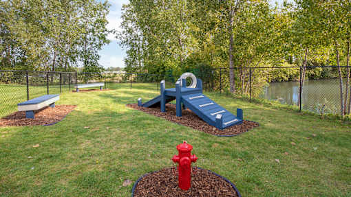 A red fire hydrant sits in a mulched area in front of a blue bench.