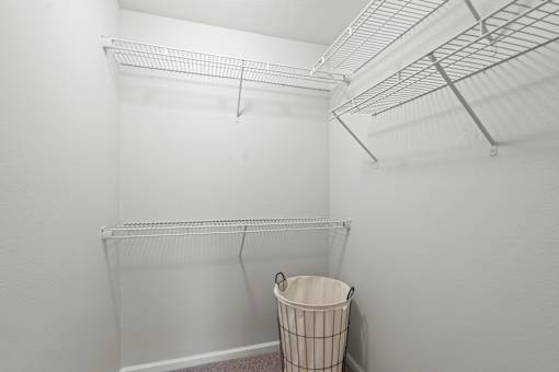 A white room with a wire shelf and a trash can.