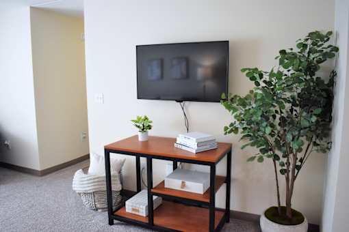 A black TV is mounted on a white wall above a black and brown table with a plant on it.