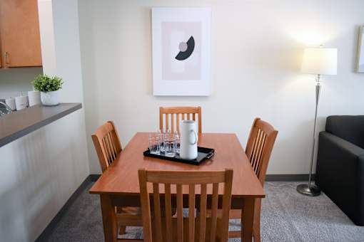 A wooden dining table with four chairs and a tray with glasses and a mug on it.