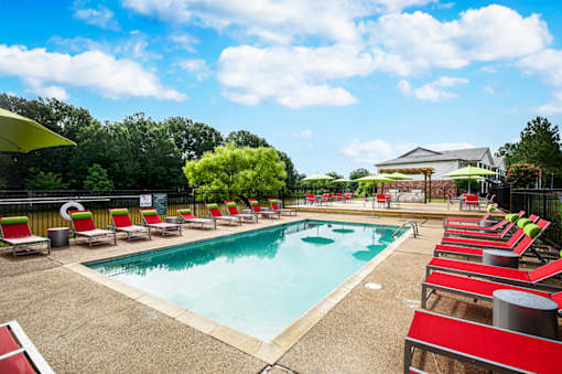 Outdoor swimming pool surrounded by red lounge chairs at Southwind Apartments in Richland, MS.