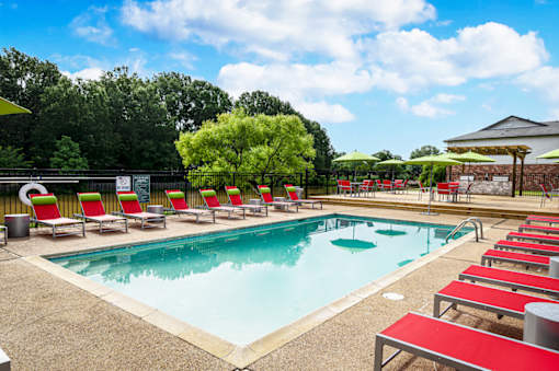 Community pool with red sun loungers and yellow umbrella at Southwind Apartments in Richland, MS.