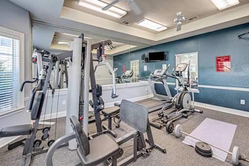 A well-equipped gym with various exercise machines and a television mounted on the wall.