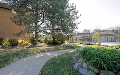 A paved walkway leads through a landscaped area with a building in the background.