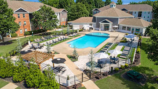 A large outdoor swimming pool surrounded by a fence and lounge chairs.