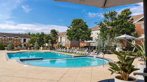 A large outdoor swimming pool surrounded by lounge chairs and trees.