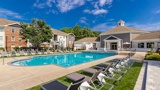 A large swimming pool surrounded by lounge chairs and buildings in the background.