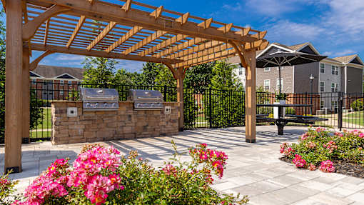 A wooden pergola is over a walkway with pink flowers.