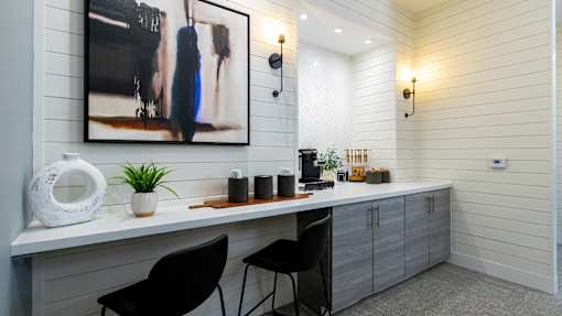 A modern kitchen with a large painting on the wall and two black chairs.