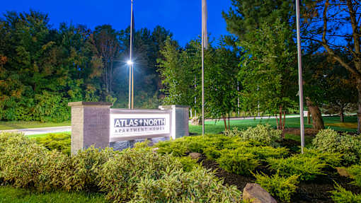 A sign for Atlas North Apartment Homes is lit up at night.