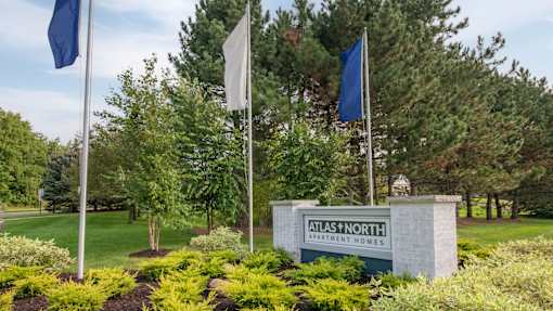 A sign for Atlas North Apartment Homes is surrounded by greenery and flags.