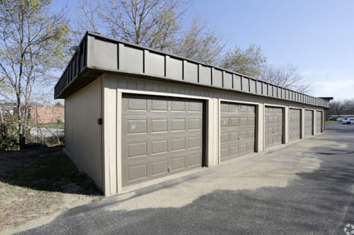 A long garage with a brown door is surrounded by trees.