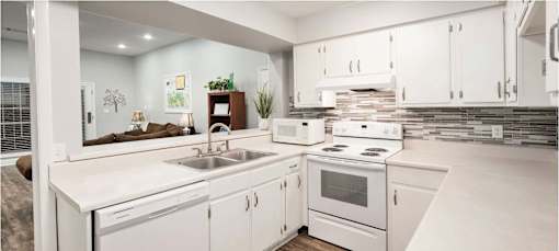 A white kitchen with a stove, sink, and cabinets.