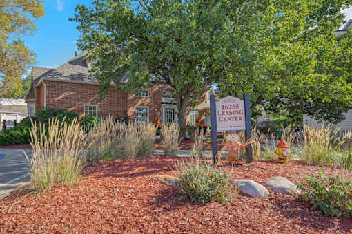 A leasing center sign is in front of a tree and a brick building.