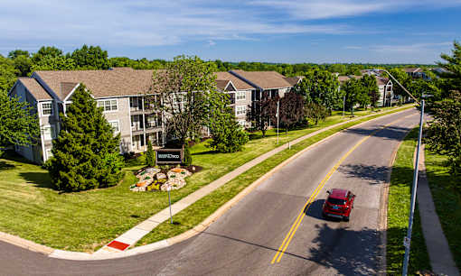 A red truck is driving down a street in front of apartment buildings.